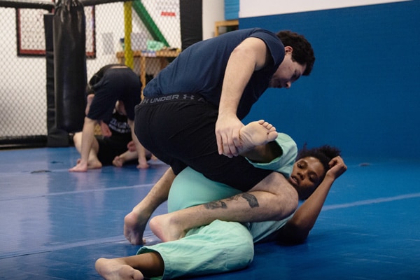 Students practicing a No-Gi Brazilian Jiu-Jitsu submission drill at Zingano Brighton, with one student setting up a triangle choke from guard while others train in the background on the blue mat.